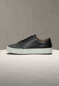 Μαύρο δερμάτινο αθλητικό παπούτσι με λεία επιφάνεια, λευκή λαστιχένια σόλα, στρογγυλή μύτη και λεπτά μαύρα κορδόνια. Το εσωτερικό διαθέτει καφέ επένδυση.