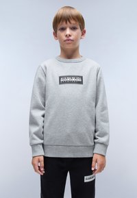 Sudadera gris con mangas largas, escote redondo y un parche de logo negro en el pecho. Combinada con pantalones negros que tienen un logo similar.