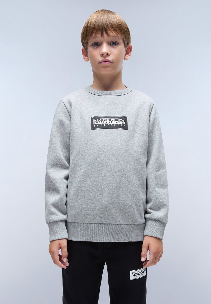 Sudadera gris con mangas largas, escote redondo y un parche de logo negro en el pecho. Combinada con pantalones negros que tienen un logo similar.