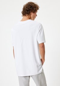 Hvid bomulds T-shirt med korte ærmer og rund hals, der har en løs pasform og glat tekstur, vist fra ryggen.