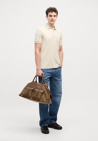 Beige polo póló és kék farmer; barna bőr sporttáska két rekesszel; fekete sportcipő. Egyszerű, laza ruházat.
