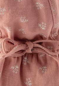 Tessuto rosa con un aspetto tessuto e texturizzato. Presenta piccoli motivi floreali bianchi e una vita cinchata con un dettaglio di nodo.