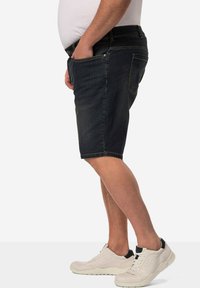 Shorts de mezclilla en azul oscuro con corte recto, que cuentan con bolsillos frontales y traseros. Combinados con zapatillas de color claro.