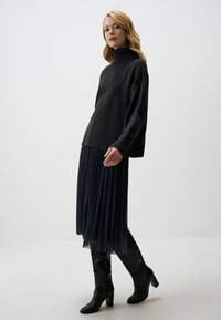 Dunkelgrauer Rollkragenpullover mit lockerer Passform und gerippten Säumen, kombiniert mit einem plissierten marineblauen Rock mit dezentem Muster und schwarzen kniehohen Stiefeln.