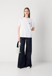 White cotton t-shirt with a small black logo, paired with wide-leg dark denim jeans and a metallic silver handbag with a black strap.