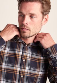 Plaid button-up shirt in navy blue, white, and orange, featuring a collar and chest pocket, made of cotton with a soft texture.