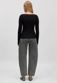 Schwarzes Langarmoberteil kombiniert mit hellgrauen, lockeren Jeans und Schuhen mit schwarz-weißen Zebra-Print. Einfaches, figurbetontes Design.
