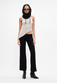 Top de tanque assimétrico bege com calças pretas com cordão; capuz de malha preto e botas de tornozelo de salto preto. Tecido texturizado, design moderno.