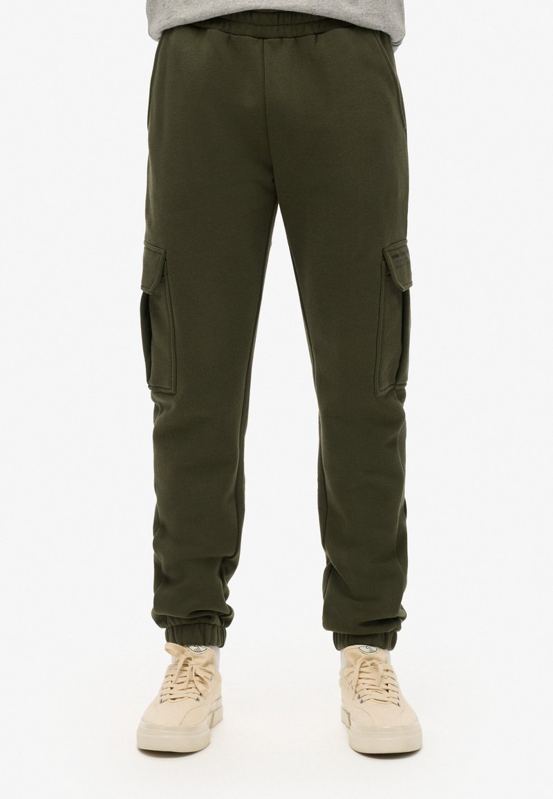 Pantalones cargo verde olivo hechos de un material suave, con bolsillos laterales, cinturilla elástica y puños. Combinados con zapatillas beige claras.