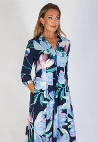 Kwiatowa sukienka w granatowym materiale, z dużymi pastelowymi wzorami kwiatowymi, z kołnierzykiem, długimi rękawami i bocznymi kieszeniami.