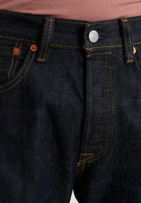 Jeans in denim blu scuro con cuciture arancioni, dotati di chiusura a bottone argentato, tasche frontali e una vestibilità classica. Tessuto liscio e strutturato.