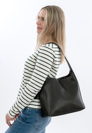 Sac en cuir noir avec une texture douce, une forme légèrement affaissée et une seule sangle, présenté sur un modèle portant un haut à rayures à manches longues.