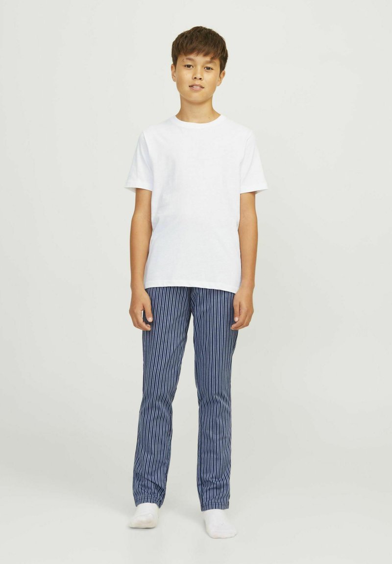 T-shirt blanc à manches courtes associé à un pantalon rayé bleu marine. Les pantalons présentent des rayures verticales et une ceinture élastique. Le modèle est pieds nus.