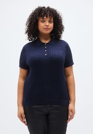 Tengerészkék kötött galléros póló texturált mintával, rövid ujjakkal és háromgombos gombolattal. Bal oldalon kis logóval rendelkezik.