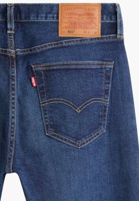 Mörkblå denimjeans med en läderetikett i midjan, bakficka med sömdekoration och en liten röd Levi's-logotyp på sidan.