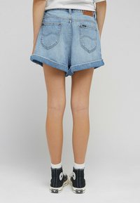 Vaaleansiniset farkkushortsit, joissa on käännetyt lahkeet, suunniteltu kahdella takataskulla ja ruskea merkkilogo vyötäröllä. Yhdistetty mustiin korkeilta varrelta oleviin tennareihin.