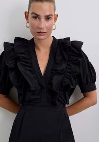 Blusa nera con grandi maniche a volant e scollatura a V profonda. Realizzata in tessuto morbido, presenta una vita aderente con una struttura definita.