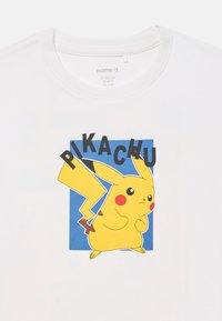 Biała bawełniana koszulka z grafiką Pikachu o żółtym futerku, czerwonych policzkach i ogonie w kształcie błyskawicy na niebieskim tle.