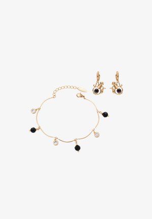 Armbånd i guldfarve med vekslende sorte og klare runde perler, kombineret med øreringe i guldfarve formet som en tekande med sorte runde sten.