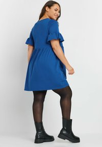 Blå kortärmad klänning med volangärmar, avslappnad passform och utsvängd kjol. Matchas med svarta ankelboots och ogenomskinliga strumpbyxor.