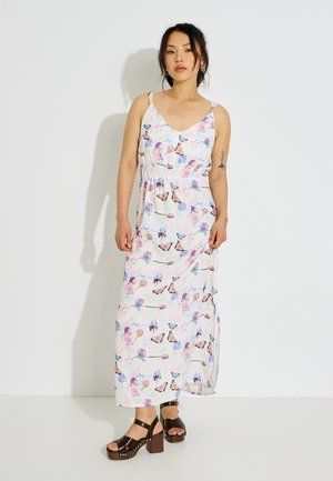 Femme portant une robe maxi blanche avec des imprimés colorés de papillons et de fleurs, assortie à des sandales plateforme marron foncé.