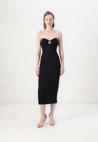 Čierne strapless šaty s priliehavým strihom, nariasenou tkaninou na poprsí a zlatým dekoratívnym sponou, siahajúcimi po stred lýtok.