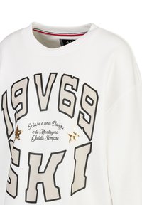 Weißes Sweatshirt mit auffälliger schwarzer und beiger Schrift, verzierten goldenen Paillettensternen und einem gerippten, gestreiften Kragen.