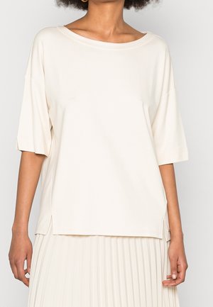 Beige top met korte mouwen in zacht materiaal, met een brede halslijn, losse pasvorm en zijsplitten voor comfort. Geen zichtbare patronen of hardware.