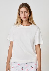 Biała bawełniana koszulka z krótkim rękawem i okrągłym dekoltem. Charakteryzuje się prostym wzorem i miękką fakturą. Noszona z wzorzystymi szortami do piżamy.