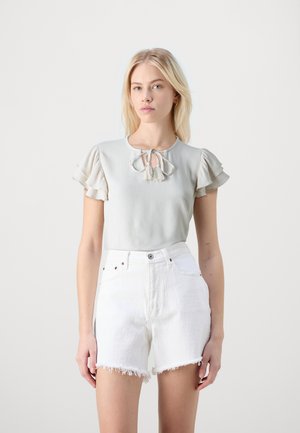 Light gray short-sleeve top with a round neckline and a tie detail featuring tassels; paired with white denim shorts with frayed hems.