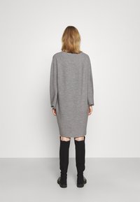 Robe tricotée grise oversize à manches longues, texture côtelée et coupe droite, associée à des bottes noires montant jusqu'aux genoux.