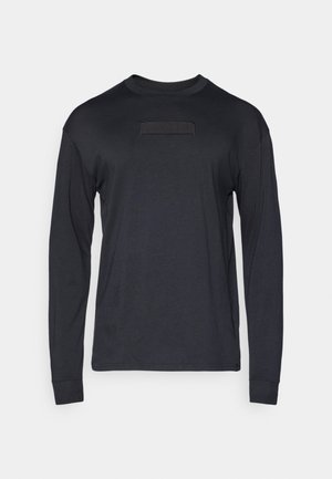 Black long-sleeve t-shirt made from soft fabric, featuring a front patch with textured detailing and a crew neckline.