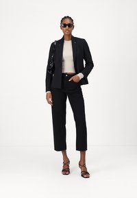 Crni sako na mjeru preko kremaste rebraste bluze, uparen s crnim skraćenim hlačama. Dodatno upotpunjen crnim naočalama za sunce i sjajnom torbicom.