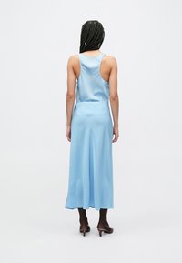 Svetlo modra maxi obleka iz satena z zadnjim dizajnom, brez rokavov in tekočo teksturo, kombinirana z rjavimi čevlji z nizko peto.