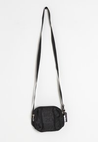 Malá černá crossbody taška s nastavitelným popruhem, zipovým uzávěrem a jemně texturovaným vzorem, visící na bílém pozadí.