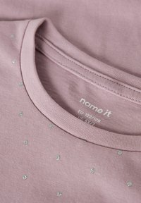 Helles rosa Baumwoll-T-Shirt mit rundem Halsausschnitt, verziert mit kleinen silbernen Strasssteinen, gleichmäßig über die Vorderseite verteilt.