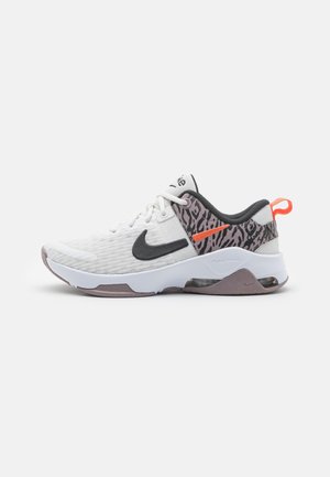 Witte lage sportschoen met zwarte Nike-swoosh, dierenprintaccenten, oranje details en zichtbare luchtvering in de zool.