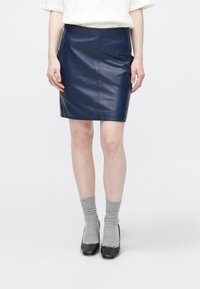 Temno modra usnjena krilo za svinčnik z gladko teksturo, oprijeto zasnovo in stranskimi šivi. Povezana s sivimi nogavicami in črnimi visokimi petami.