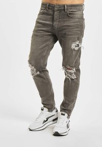 Gray ripped jeans with frayed edges, slim fit, five-pocket design, paired with white sneakers featuring black accents.