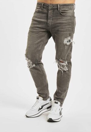 Jeans rasgados grises con bordes deshilachados, ajuste slim, diseño de cinco bolsillos, combinados con zapatillas blancas con detalles en negro.