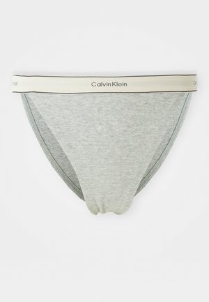 Svijetlosivi muški slip gaćice s bijelim elastičnim pojasom na kojem se nalazi crni natpis "Calvin Klein".