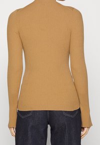 Bruine geribbelde langermige top met een aansluitende silhouet en hoge hals, met een gestructureerde stof en een sleek, minimalistisch ontwerp.