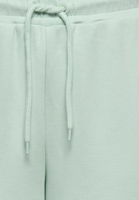 Svetlo zelene joggerske hlače z zategovalnim trakom v pasu, iz mehke tkanine, z gladko teksturo brez vidnih vzorcev.
