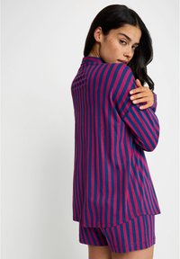 Conjunto de roupa de lazer listrado em roxo e fúcia, apresentando uma blusa de manga longa com gola e calções combinando. Material de algodão suave.