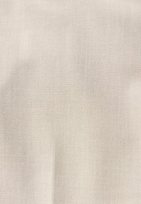 Tissu beige texturé avec un motif tissé subtil en forme de grille et de légers plis ombragés sur toute sa surface.