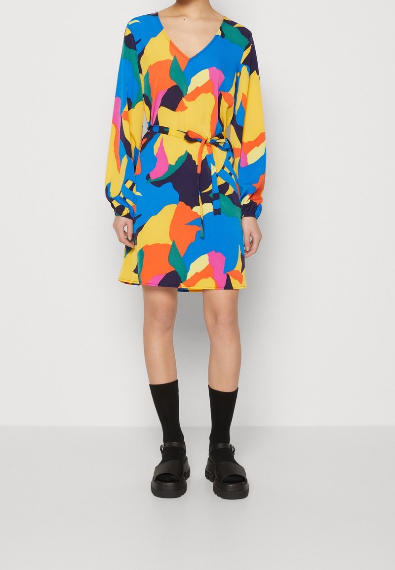 Robe colorée à col en V avec des manches longues, une taille cintrée avec un lien, et un motif abstrait audacieux en bleu, jaune, orange et vert.