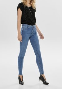 Top corto de estampado de leopardo negro, jeans ajustados de talle alto en azul y zapatos de tacón negro brillante con acentos texturizados.