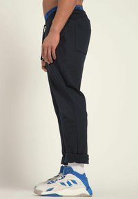 Marine joggingsbroek met een trekkoord in de taille en opgerolde manchetten, met een achterzak, gecombineerd met blauw en witte sportschoenen.