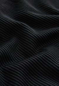 Black ribbed fabric with subtle wave pattern, showing soft texture and depth. The folds create shadows, emphasizing the material's flexibility.