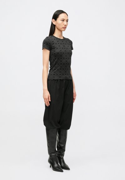 Top preto de manga curta com textura padronizada, combinado com calças pretas largas e botas pretas de couro até ao joelho, design minimalista.